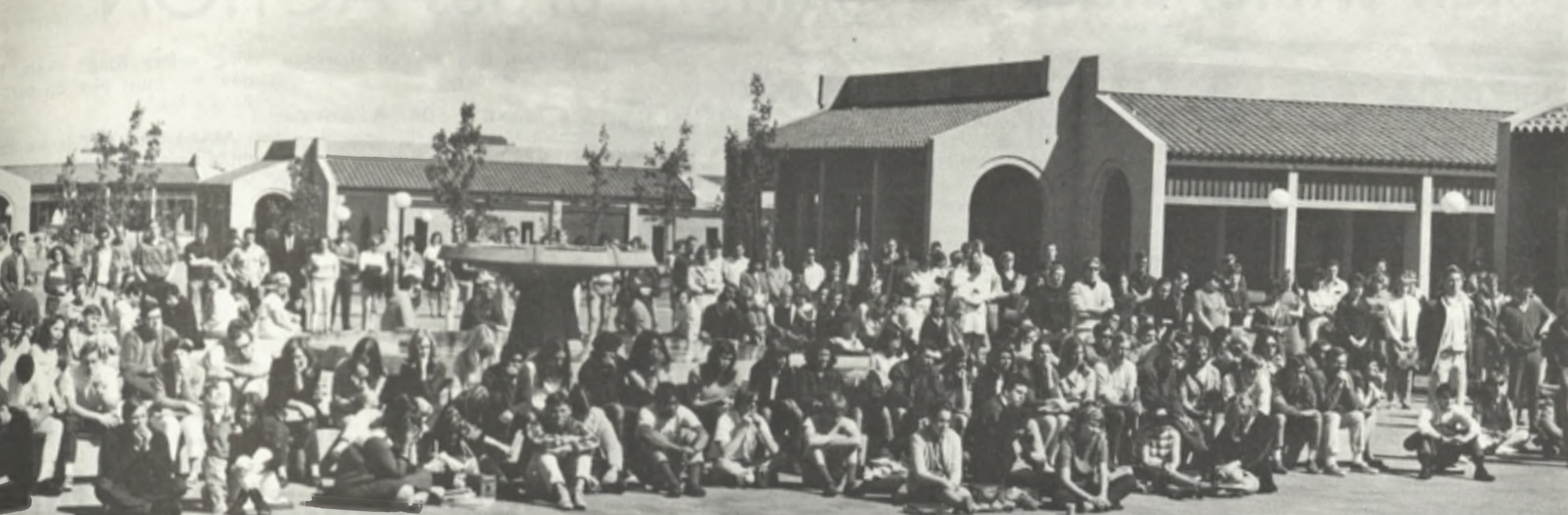 De Anza students gathered to pay tribute to the late Martin Luther King Jr. following his assassination (La Voz, April 1968) A large group of people, seated and standing, is gathered outdoors in front of a series of buildings with tiled roofs