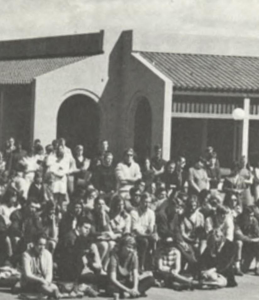 MLK gathering (La Voz, 1968) A large group of people, seated and standing, is gathered outdoors in front of a series of buildings with tiled roofs