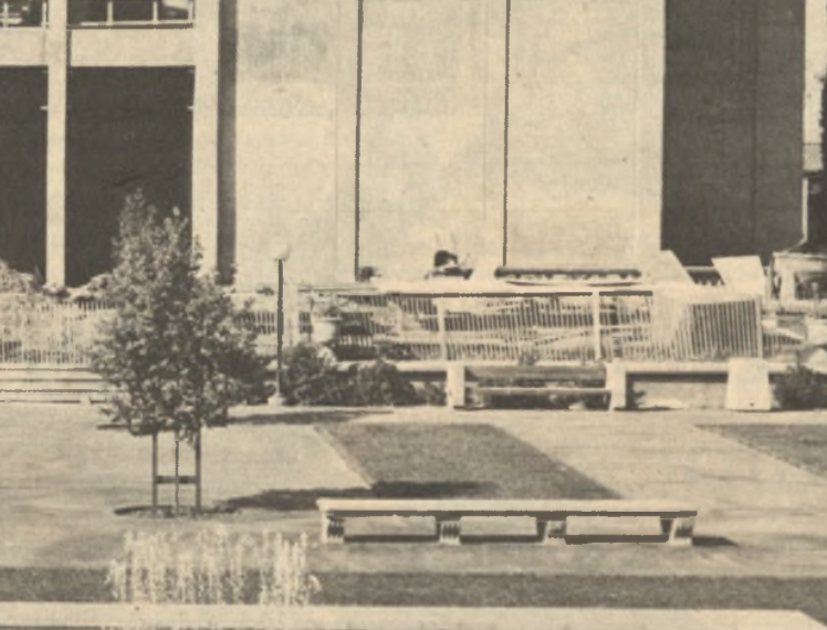 An empty De Anza campus (La Voz circa 1985) A black and white photo of an empty plaza with a tree next to a concrete bench. Fences and buildings are visible in the background.
