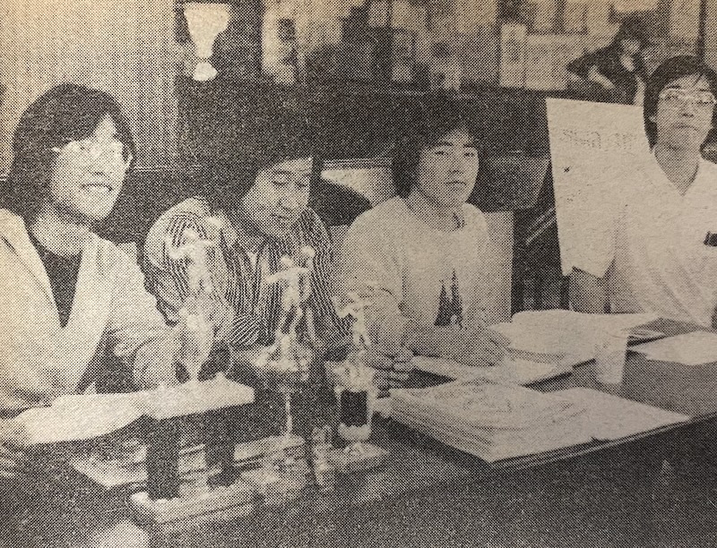 Members of De Anza's Asian Club. (La Voz, 1980) Four students sit at a table with trophies and papers in front of them.