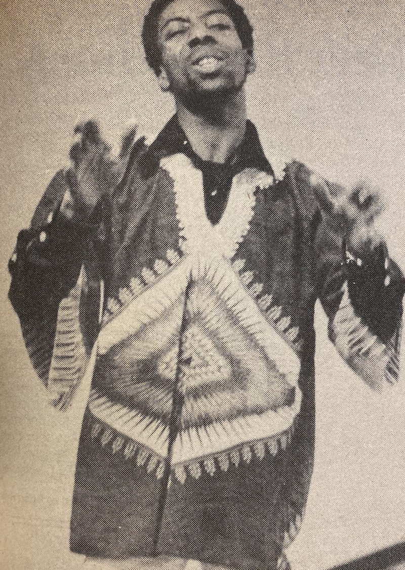 An artist performs during Black Heritage Month. (La Voz, 1980) A Black man wearing a patterned shirt gestures with their hands, appearing expressive. The shirt features intricate geometric designs.