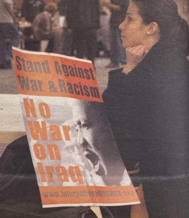 A woman holds a protest sign that reads "Stand Against War & Racism. No War on Iraq."