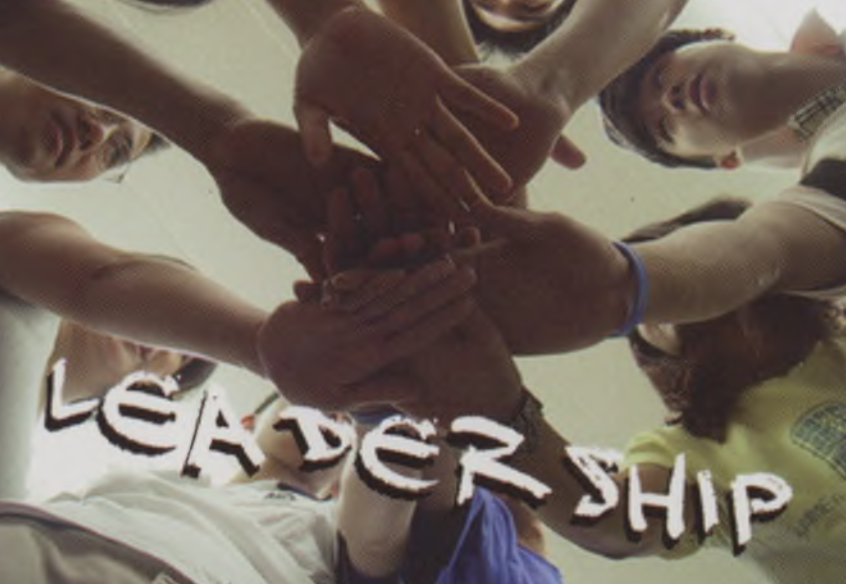 A group of people standing in a circle, reaching in to place their hands together in the center. The word Leadership is displayed diagonally in bold letters at the bottom.