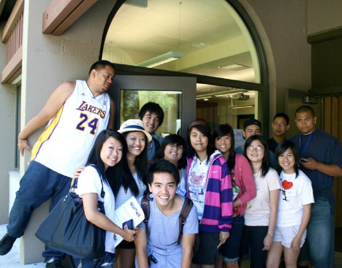 A group of smiling young adults poses in front of a building entrance.