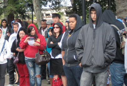 A large group of people wearing hoodies and jackets stand outdoors.