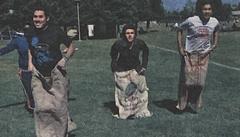 Three people are participating in a sack race on a grassy field.