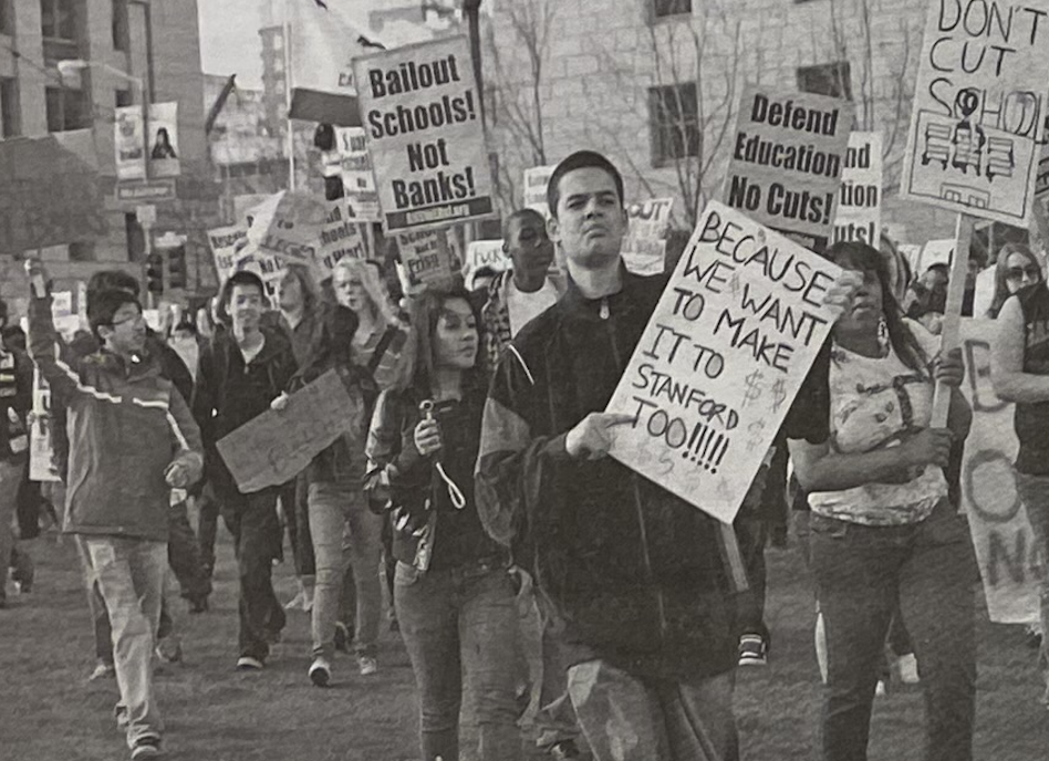 A group of protesters marches while holding signs. One prominent sign reads, Because we want to make it to Stanford too! Other signs advocate for education funding and express discontent with bank bailouts.