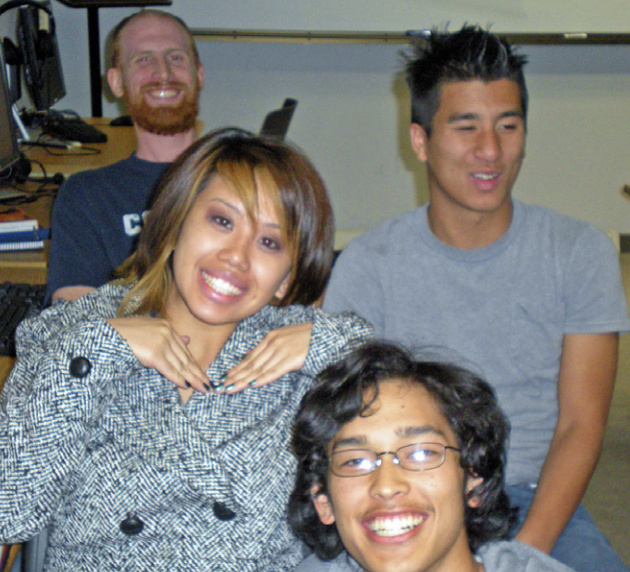 Four people are smiling in a classroom setting.