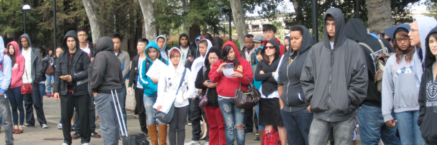 A large group of people wearing hoodies and jackets stand outdoors.