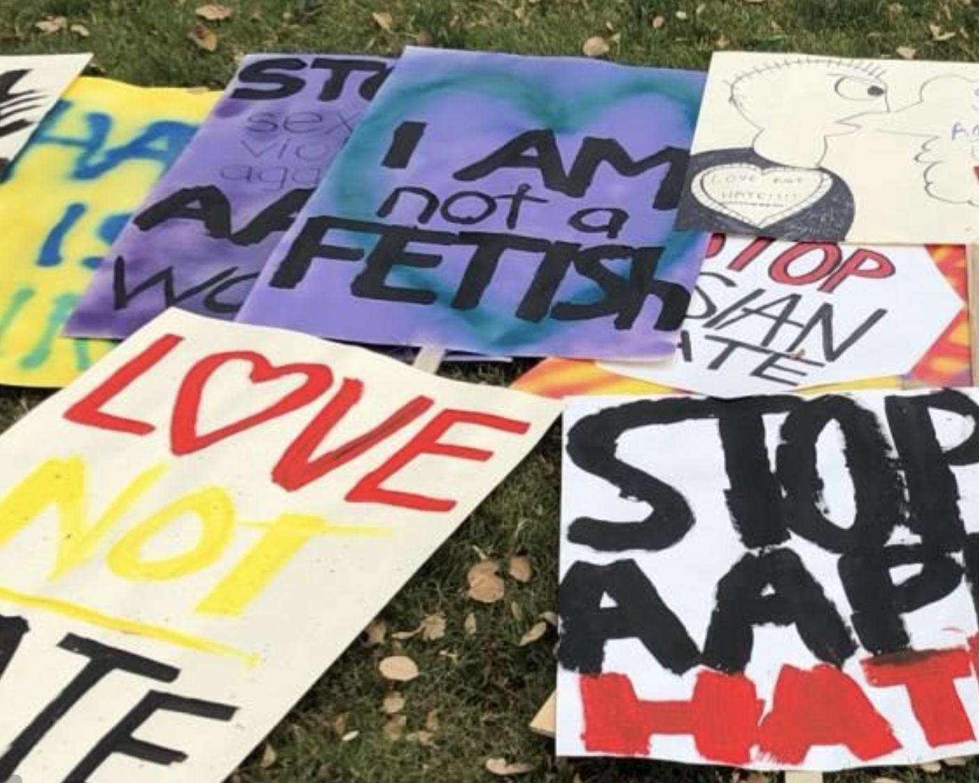 Show thumbnail preview A collection of protest signs lay on the grass. Messages include I am not a fetish, Stop Asian hate, Love not hate, and other similar phrases in bold colors. 