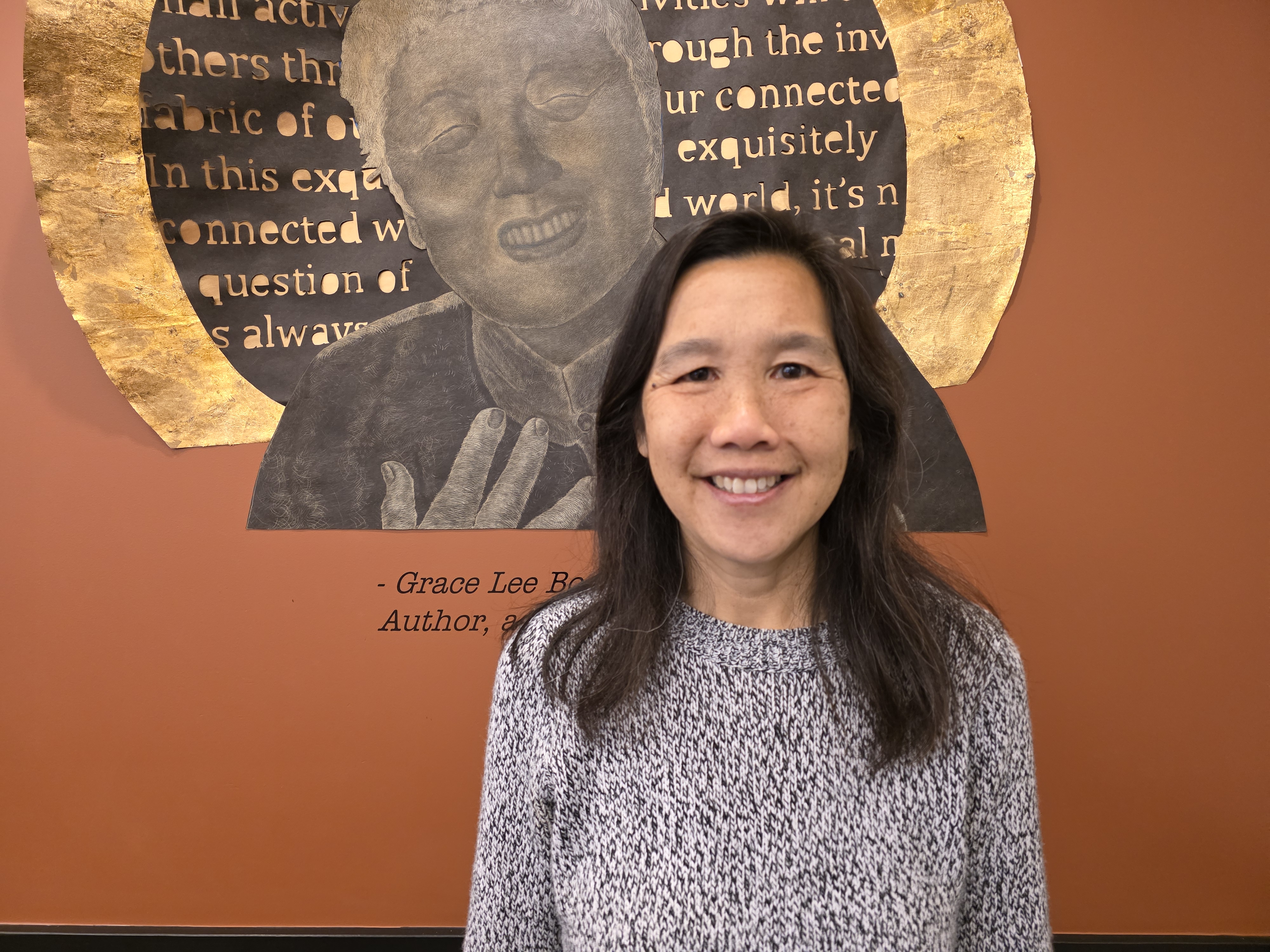 A person with long dark hair is smiling while standing in front of an indoor mural.