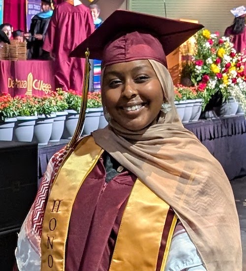 smiling young woman in cap and gown and Honors sash