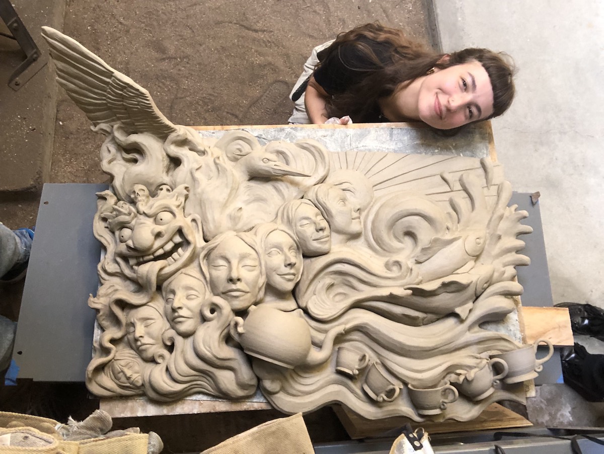 photo of young woman holding face sideways alongside ceramic sculpture
