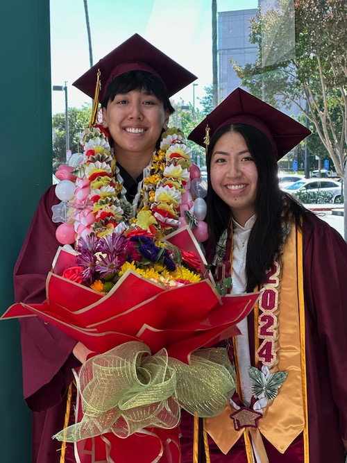 smiling young man and young woman in grad regalia and flowers