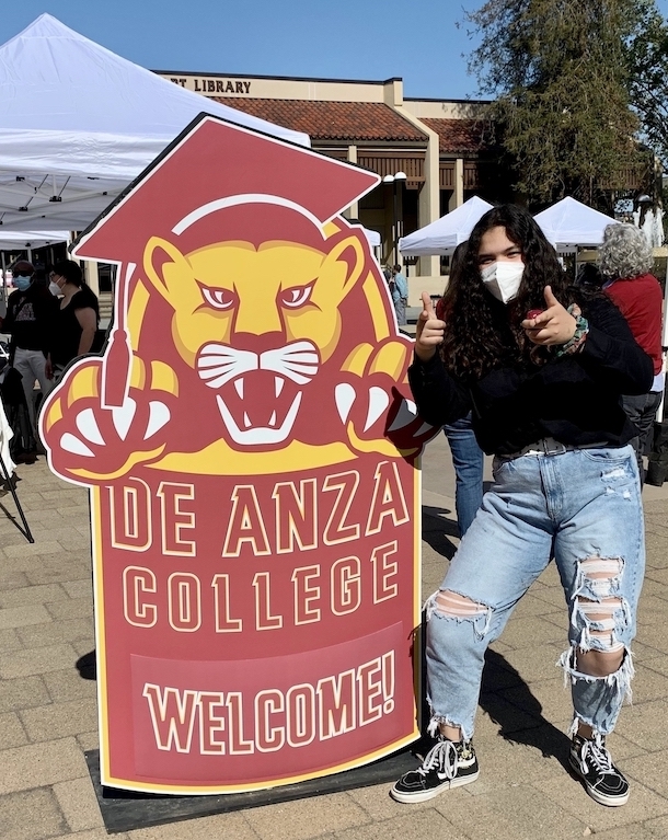 young woman wearing face mask and ripped jeans giving thumbs up next to mountain lion cutout