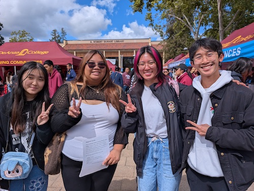 four students smiling in front of tents in Main Quad 
