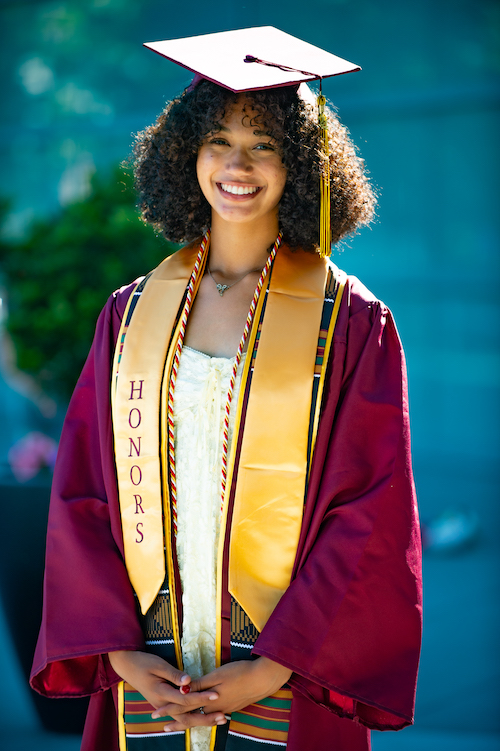 young woman with honors sash and grad cap and gown